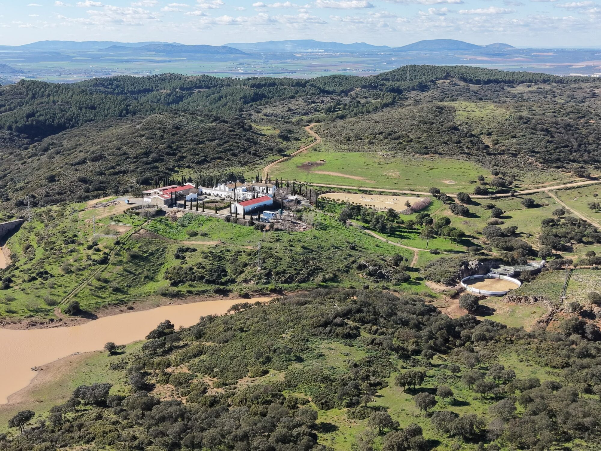 Aerial view of the whitewashed La Toro Estate cortijo set among oak woodland beside a river